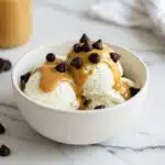 bowl of creamy cottage cheese ice cream topped with chocolate chips and a drizzle of peanut butter