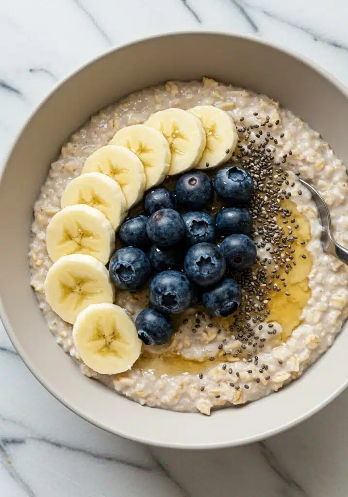high-protein oatmeal on a marble countertop, topped with sliced banana, blueberries, a drizzle of honey