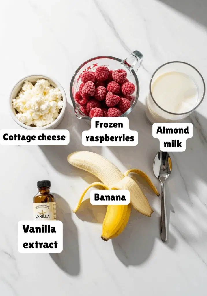 Ingredients for raspberry cottage cheese smoothie on a marble countertop.