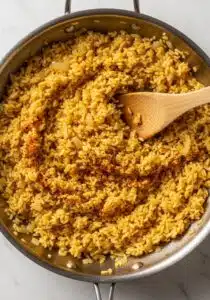 Pan filled with fluffy, golden Cajun-spiced rice being stirred with a wooden spatula